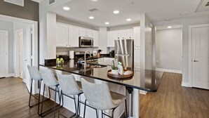 A modern kitchen with a central island, bar stools, stainless steel appliances, and a clean, minimalist design. - Modern 3-bed, 2-bath condo minutes from Disney! (Kissimmee)