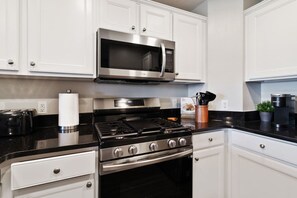 A modern kitchen with white cabinets, a stainless steel stove, a microwave, and a coffee maker. - Modern Golf View Oasis: Close to Parks! (Kissimmee)