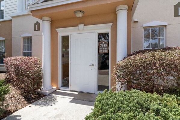 A building entrance with a white door, columns, and a sign indicating unit numbers. - Modern Golf View Oasis: Close to Parks! (Kissimmee)
