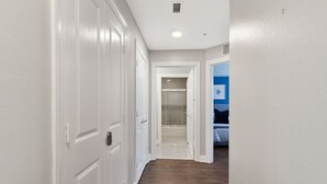 A hallway with white doors, a shower area, and a bedroom with a bed and a blue wall. - Modern 3-bed, 2-bath condo minutes from Disney! (Kissimmee)