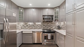 A modern kitchen with stainless steel appliances, a tiled backsplash, and light-colored cabinetry.