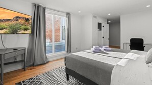 A modern bedroom with a large bed, a desk, and a TV on the wall.