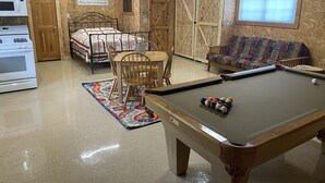 Una habitación acogedora con mesa de billar, cama, sofá y rinconcito de cocina.