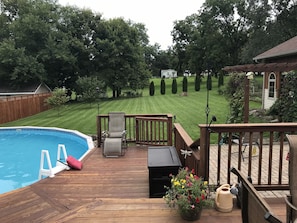 A backyard with a swimming pool, wooden deck, and a lawn.