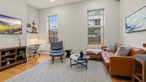 A living room with a sofa, a chair, a coffee table, a TV, and a bookshelf. - Beautiful 1BD With Balcony | Rittenhouse Square (Philadelphia)