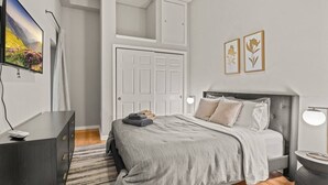 A bedroom with a bed, a TV, a wardrobe, a door, and two framed pictures on the wall. - Beautiful 1BD With Balcony | Rittenhouse Square (Philadelphia)