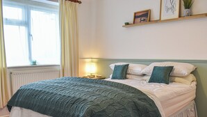 A neatly made bed with a green quilt, a bedside lamp, and a shelf with decorative items. - 2 bedroom accommodation in Canonstown (Canonstown)