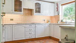 A kitchen with white cabinets, a tiled backsplash, and a window with a view of greenery. - 2 bedroom accommodation in Canonstown (Canonstown)