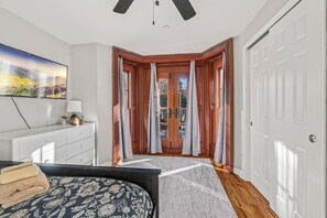 Een slaapkamer met een bed, een bureau, een stoel, een raam met gordijnen en een deur.