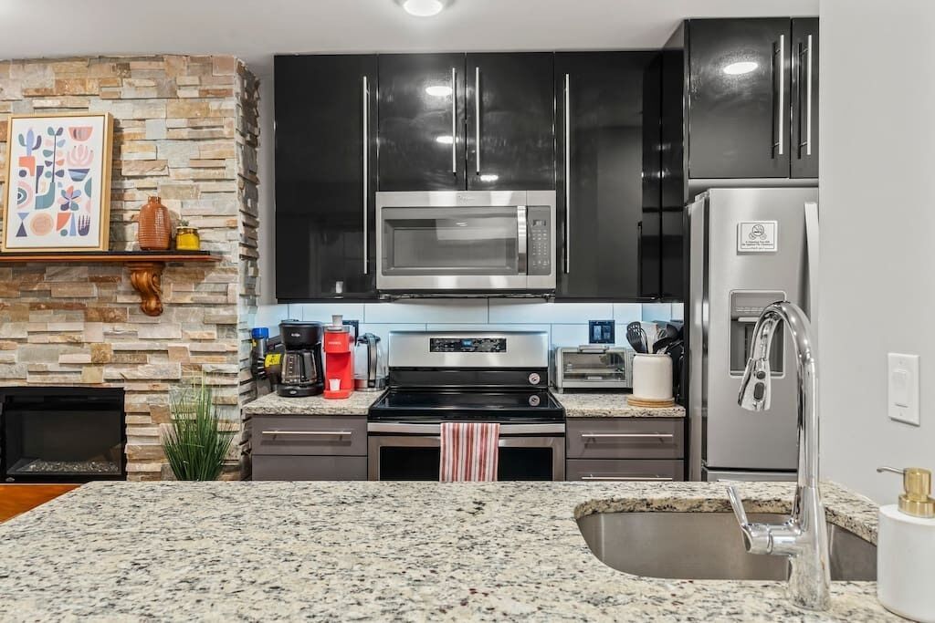 Een keuken met granieten aanrecht, een ingebouwde magnetron, een roestvrijstalen oven, een koelkast en een backsplash van natuursteen.