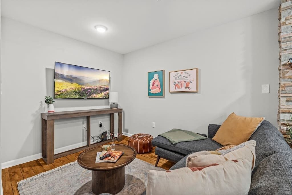 A living room with a sofa, ottoman, coffee table, and artwork on the wall.