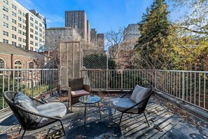 A rooftop terrace with outdoor seating, a view of the cityscape, and a metal fence.
