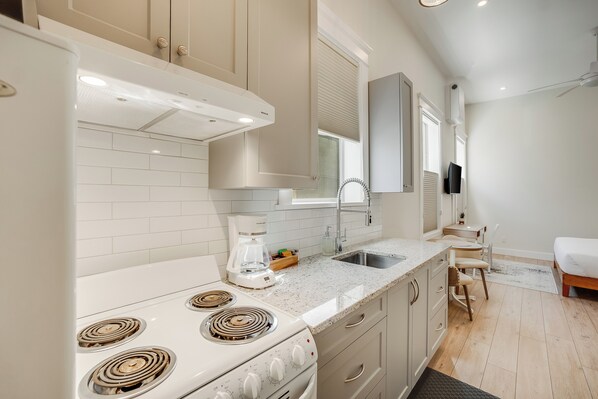 A modern kitchen with a stove, sink, and a dining area with a chair and table.