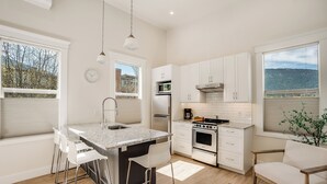 A modern kitchen with a central island, white cabinetry, stainless steel appliances, and large windows offering views of the outdoors. - Stirling All Suites Hotel (Nelson)