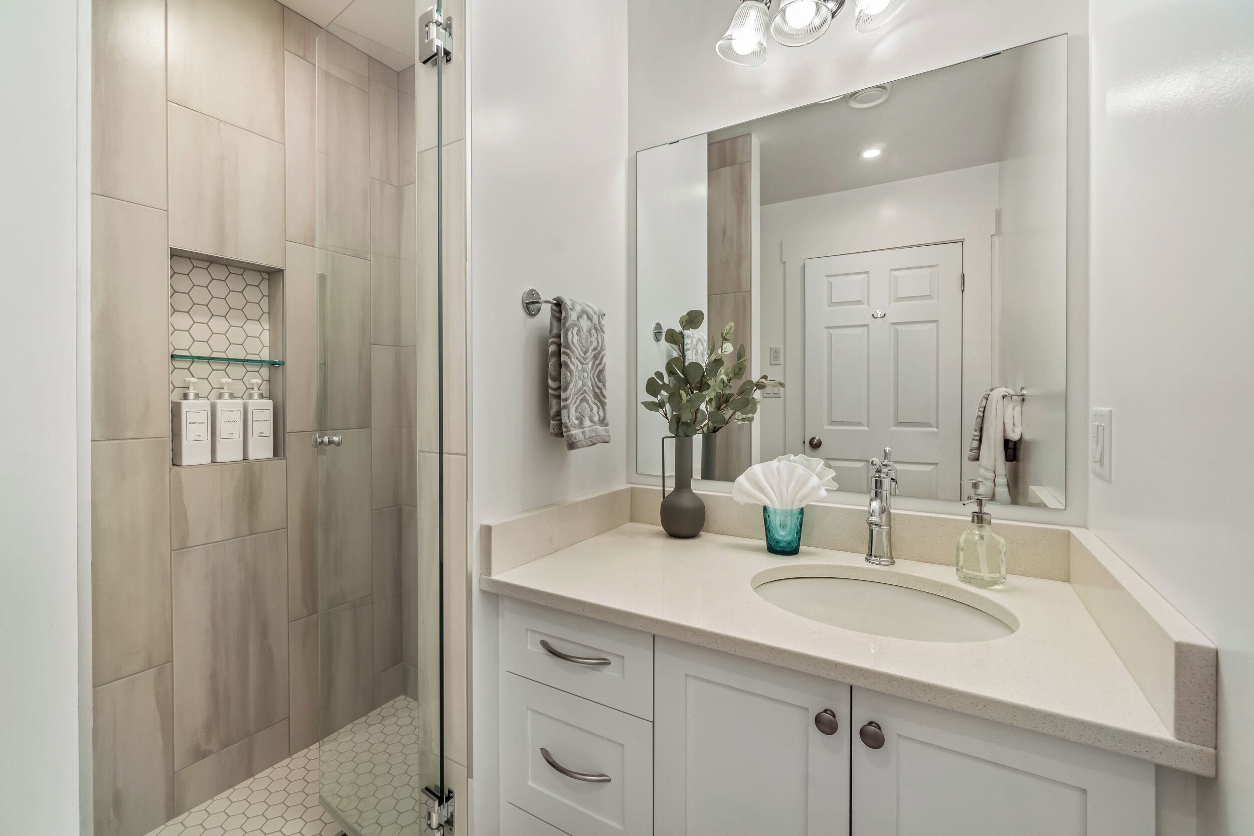 A modern bathroom with a glass shower enclosure, a large mirror, and a sink with a vase of flowers.