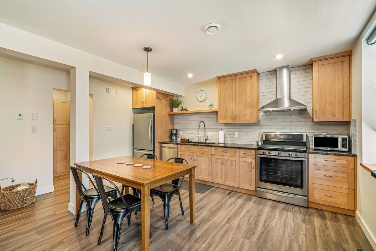 Una cocina moderna con armarios de madera, electrodomésticos de acero inoxidable y una zona de comedor con mesa y sillas de madera.