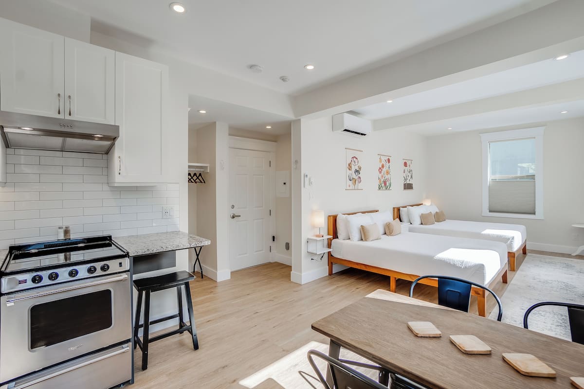 Una cocina moderna con estufa y armarios, un comedor con mesa y sillas, y un dormitorio con dos camas y una ventana.
