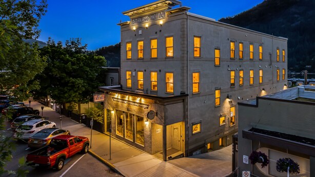 A two-story building with a sign reading "Stirling Hotel." It features a ground-level entrance with a glass facade and a parking lot in front. - Stirling All Suites Hotel (Nelson)