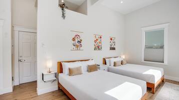 A bedroom with two beds, a white door, a small bedside table with a lamp, and wall art.