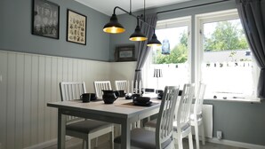 Un comedor con una mesa y sillas blancas, detalles decorativos en blanco y negro en la pared, y vistas al exterior a través de grandes ventanales.