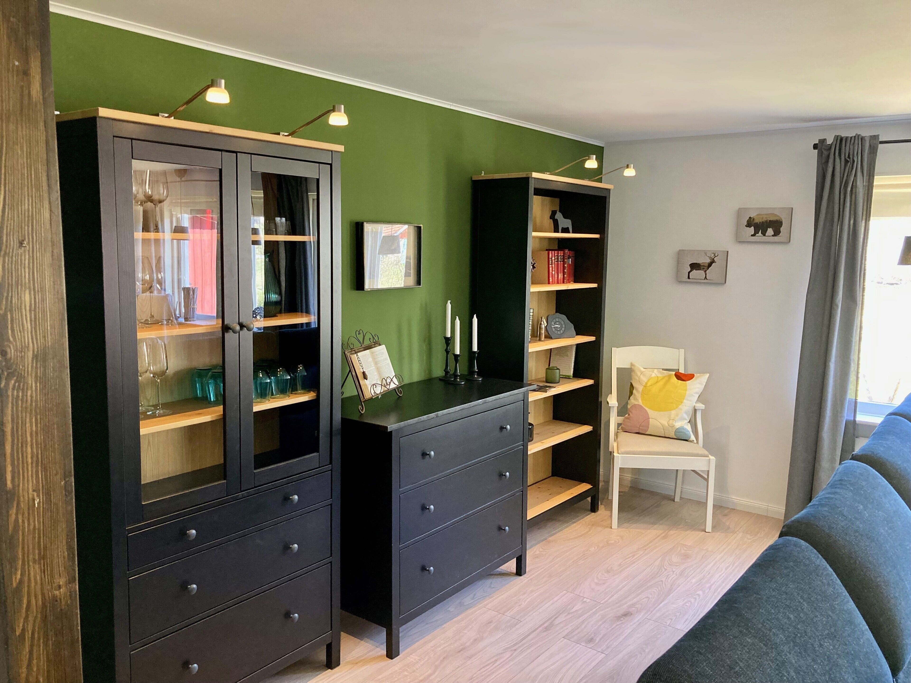 Un salon moderne avec un mur d’accent vert, deux meubles en bois foncé dotés de portes en verre, un fauteuil blanc et un canapé bleu.
