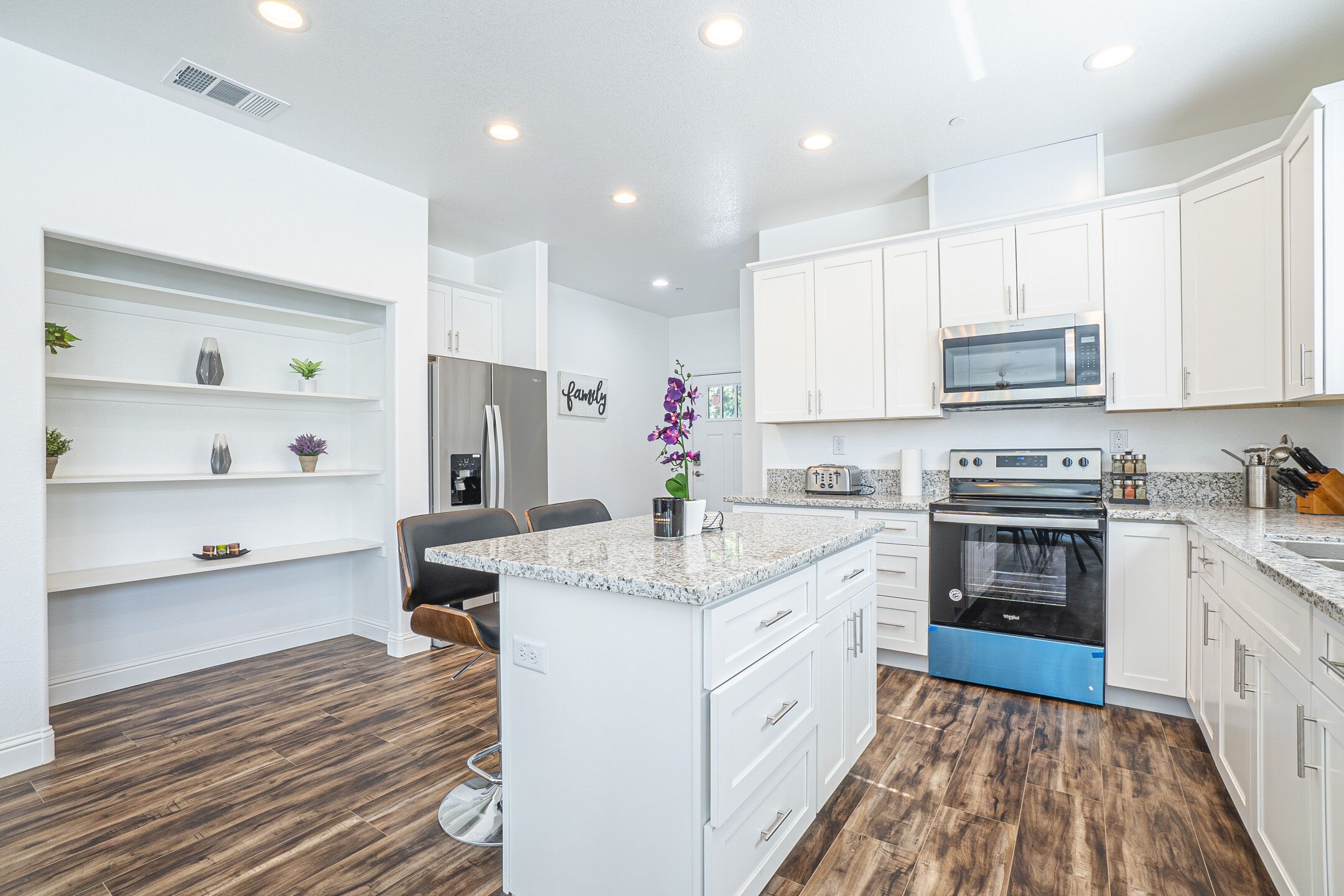A modern kitchen with white cabinetry, a central island, a built-in oven, and a microwave.