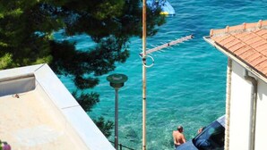 A coastal view with a clear blue sea, a person in the water, and a building with a tiled roof. - Remarkable 2-bed Apartment in Tribunj, Best View (Tribunj)
