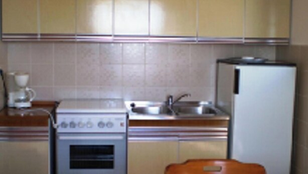 A small kitchen with a stove, sink, and refrigerator. There is a wooden chair and a table in the foreground. - Remarkable 2-bed Apartment in Tribunj, Best View (Tribunj)