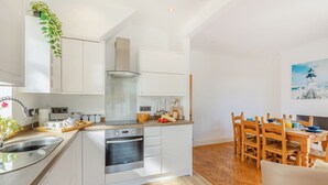 Une cuisine moderne avec des meubles blancs, un four encastré et un coin repas comprenant des chaises et une table en bois.
