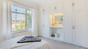 Une chambre avec une grande fenêtre, une armoire blanche et un lit avec une literie à rayures.