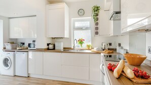 Une cuisine moderne avec des meubles blancs, un lave-linge encastré, une machine à café et un plan de travail en bois sur lequel sont disposés des produits frais.