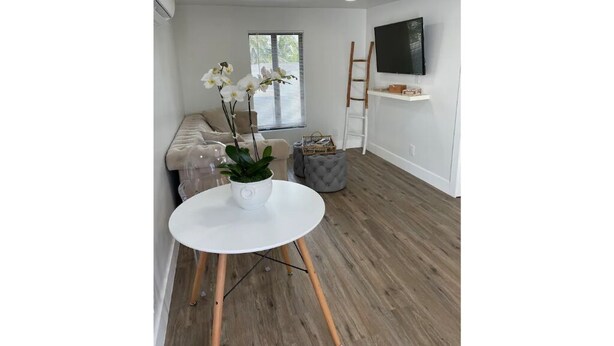 Ein modernes Wohnzimmer mit einem weißen runden Tisch, einem beigen Sofa, einem grauen Hocker und einem an der Wand befestigten Fernseher.