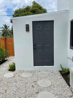 A modern house with a dark grey door, a small garden with pebbles and plants, and a wooden fence in the background.