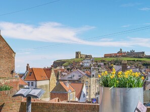 A historic town with a prominent castle on a hill, traditional buildings, and a metal sign with a flower pot.