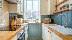 Eine kompakte Küche mit Fenster, Holzausziehtisch, einem eingebauten Backofen und Spüle.