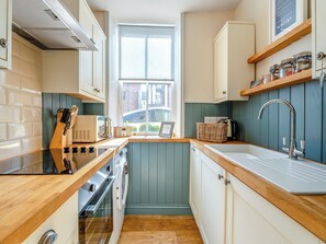 A compact kitchen with a window, wooden countertops, a built-in oven, and a sink.