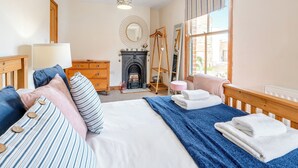 Ein Schlafzimmer mit Bett, Schminktisch, Spiegel, Kamin und großem Fenster.