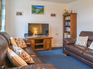 A living room with a TV, two sofas, a bookshelf, and framed pictures on the wall.