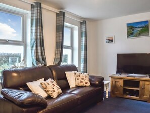 A living room with a brown leather sofa, two patterned pillows, a television on a wooden stand, and a painting on the wall.