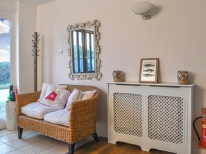 A wicker chair with white cushions, a decorative mirror, a fireplace with a lattice front, and a framed fish picture above it.