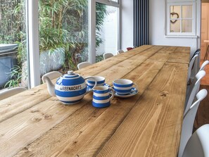A wooden table with a tea set, white chairs, and a view of greenery outside.