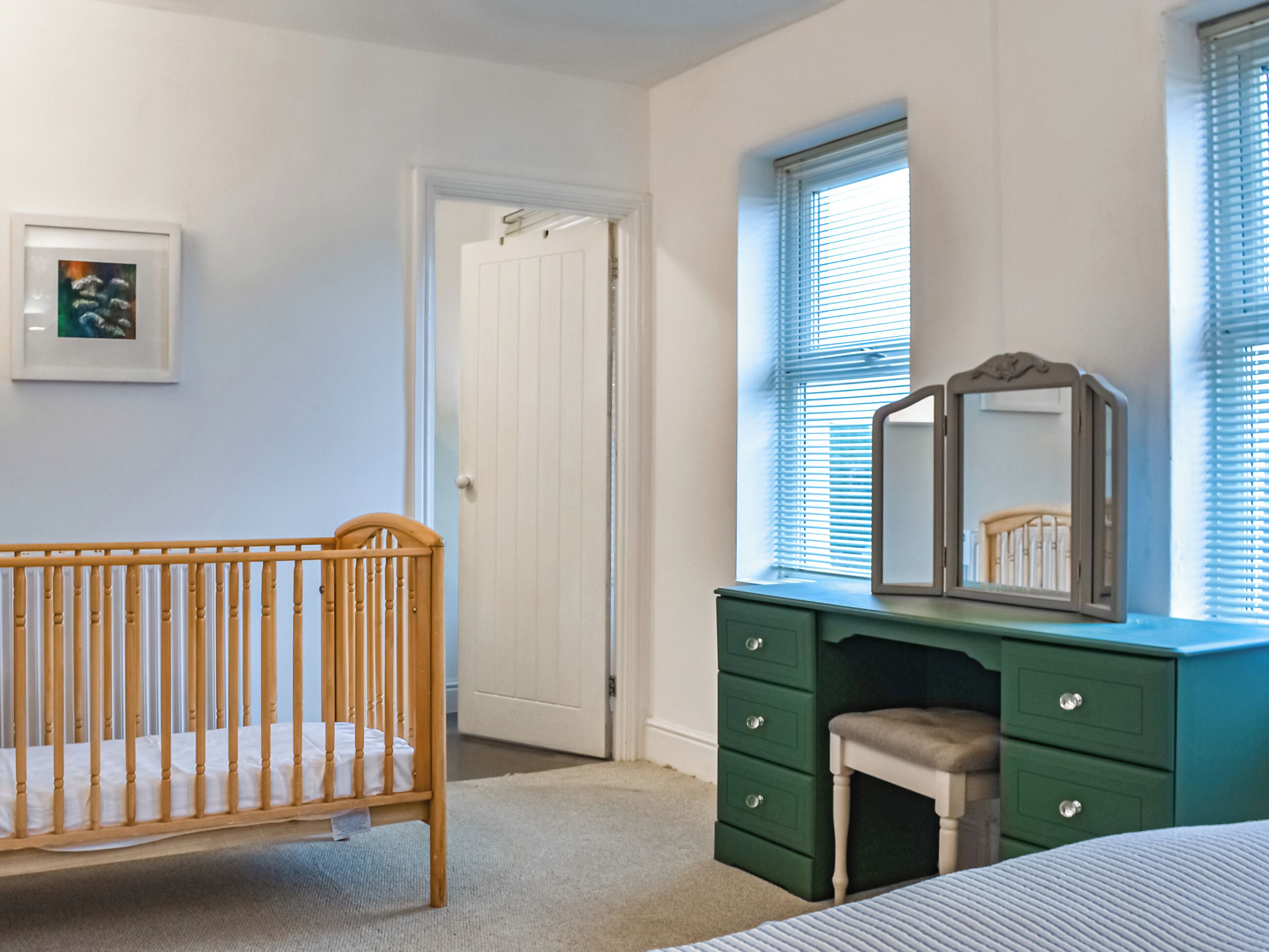 A bedroom with a crib, a dresser, a mirror, and a door.