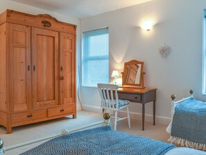 Un dormitorio con un armario de madera, un escritorio con espejo, una silla y dos camas con ropa de cama estampada.