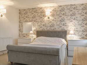 A bedroom with a bed, two bedside tables with lamps, a radiator, and a patterned wallpaper.