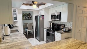 Une cuisine moderne dotée d’un îlot central, d’appareils électroménagers en acier inoxydable et d’un ventilateur de plafond.