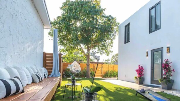 Een modern terras buiten met een houten bankje, een kleine ronde tafel en een potplant.