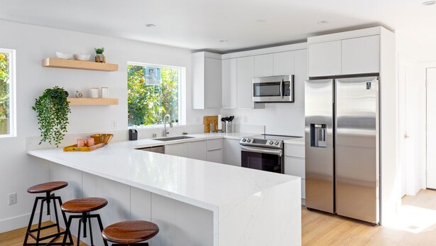 A modern kitchen with white cabinetry, stainless steel appliances, a large island with stools, and a window with a view of greenery.