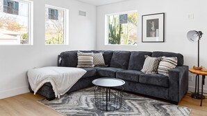 A modern living room with a dark grey sectional sofa, a round coffee table, and a patterned rug.