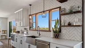 A modern kitchen with white cabinetry, stainless steel appliances, and a large window offering a view of the outdoors. - Nestled in the beautiful desert of Tucson, this home will take your breath away. (Tucson)