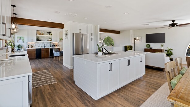 A modern kitchen with white cabinetry, a large island, and a dining area with a wooden table. - Nestled in the beautiful desert of Tucson, this home will take your breath away. (Tucson)